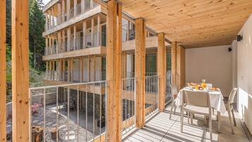 A multi-level wooden structure with balconies, a dining area with a table and chairs, and a view of the surrounding landscape.