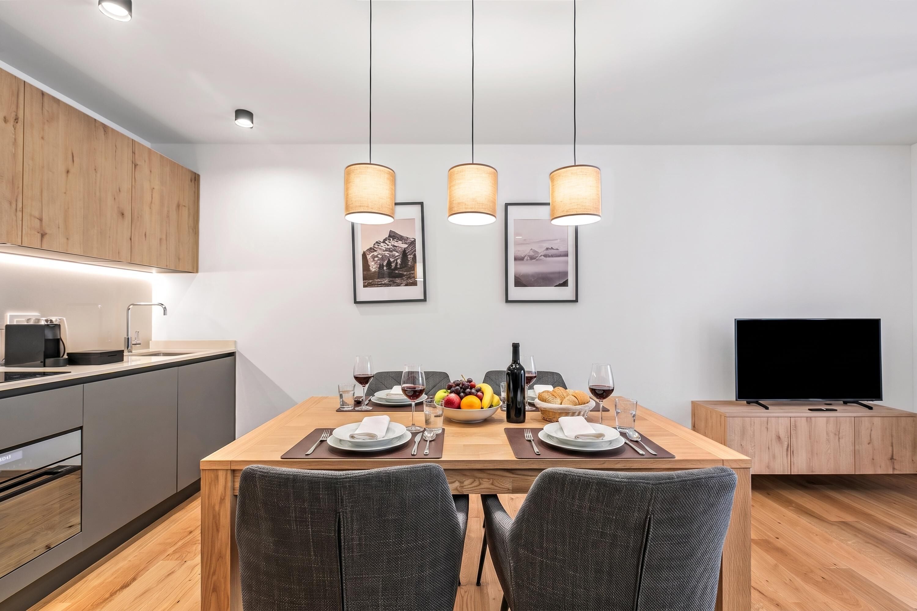 A modern kitchen with a dining area, wooden cabinets, a coffee machine, and a flat-screen TV.
