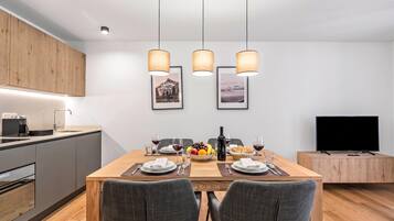 A modern kitchen with a dining area, wooden cabinets, a coffee machine, and a flat-screen TV.