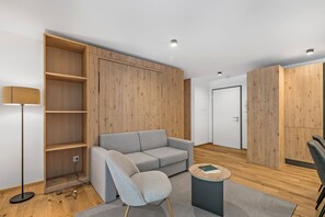 Een moderne woonkamer met een grijze bank, een klein rond tafeltje en ingebouwde houten planken.