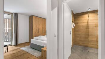 A modern bedroom with a wooden wardrobe, a bed with white linens, a small bedside table, and a grey rug.