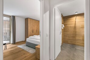 Un dormitori modern amb un armari de fusta, un llit amb roba de llit blanca, una petita taula de nit i una catifa gris.