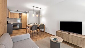 A modern living room with a flat-screen TV, a grey sofa, and a dining area with a wooden table and chairs. - Residenza Castanea 107 Modern Alpine Stay in San Bernardino | Ski, Hiking & Nature, San Bernardino, Switzerland (San Bernardino)