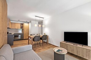 Un salon moderne avec un téléviseur à écran plat, un canapé gris et un coin repas comprenant une table et des chaises en bois.