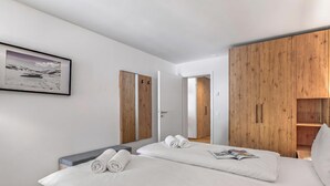 A hotel room with a bed, a gray bench, wooden wardrobe, and a framed picture on the wall. - Residenza Castanea 107 Modern Alpine Stay in San Bernardino | Ski, Hiking & Nature, San Bernardino, Switzerland (San Bernardino)