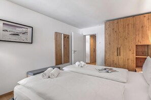 Une chambre d’hôtel avec un lit, un banc gris, une armoire en bois et un tableau encadré au mur.