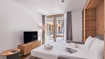 A hotel room with a bed, a television, a wooden cabinet, and a view of the outside.