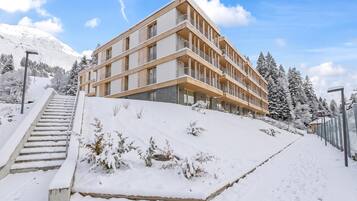 Ett hotell med flera våningar och modern design, beläget på en snötäckt sluttning, med en trappa som leder upp till entrén.