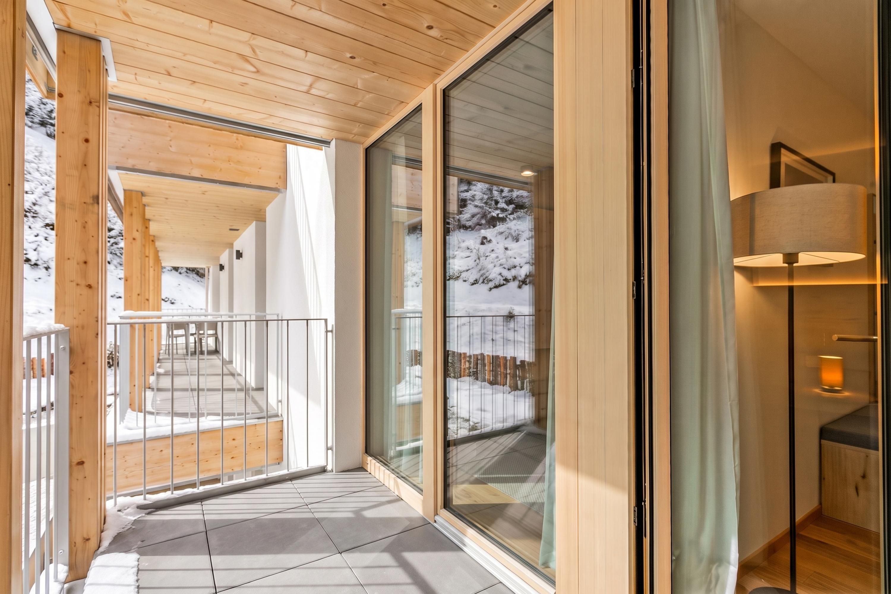 Et moderne interiør med træloft, en glasdør der fører til et sneklædt område udenfor, og et gulv-til-loft vindue.