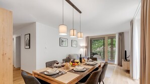 Ein moderner Essbereich mit einem Holztisch, gedeckt für sechs Personen, umgeben von Stühlen, mit Pendelleuchten darüber.