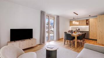 Een moderne woonkamer met een flatscreen televisie, een bank en een eethoek met een tafel voor vier personen.