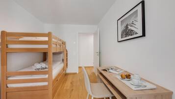 A room with a bunk bed, a desk with a chair, a framed picture on the wall, and a door leading to another room.