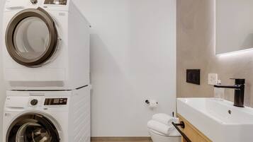 Ein kleiner Waschraum mit einer Waschmaschine und einem Trockner mit Frontlader, einer Toilette und einem Waschbecken mit modernem Wasserhahn.