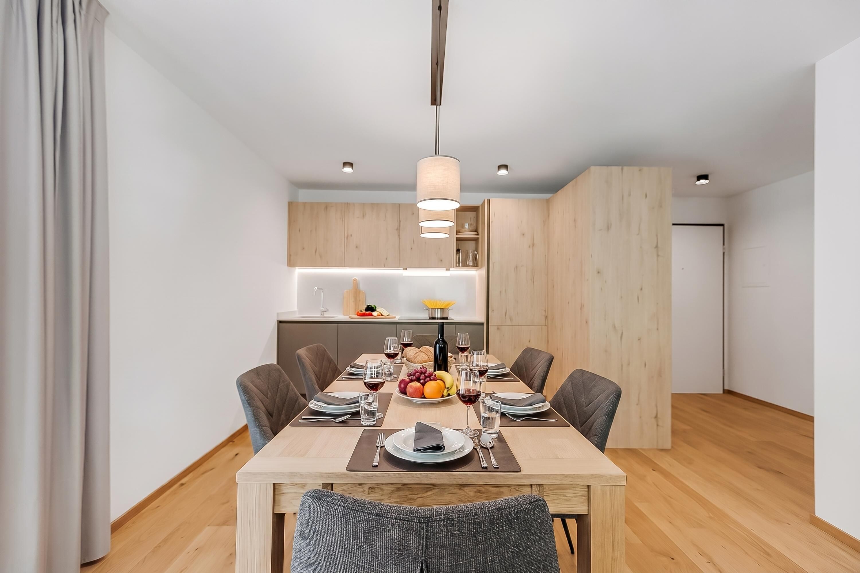 A modern dining area with a wooden table set for four, surrounded by chairs, in a room with wooden flooring and walls.