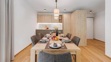 A modern dining area with a wooden table set for four, surrounded by chairs, in a room with wooden flooring and walls.