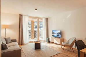 Sala moderna com sofá, mesa de centro, TV em um armário de madeira e vista para uma paisagem nevada através das portas de vidro.