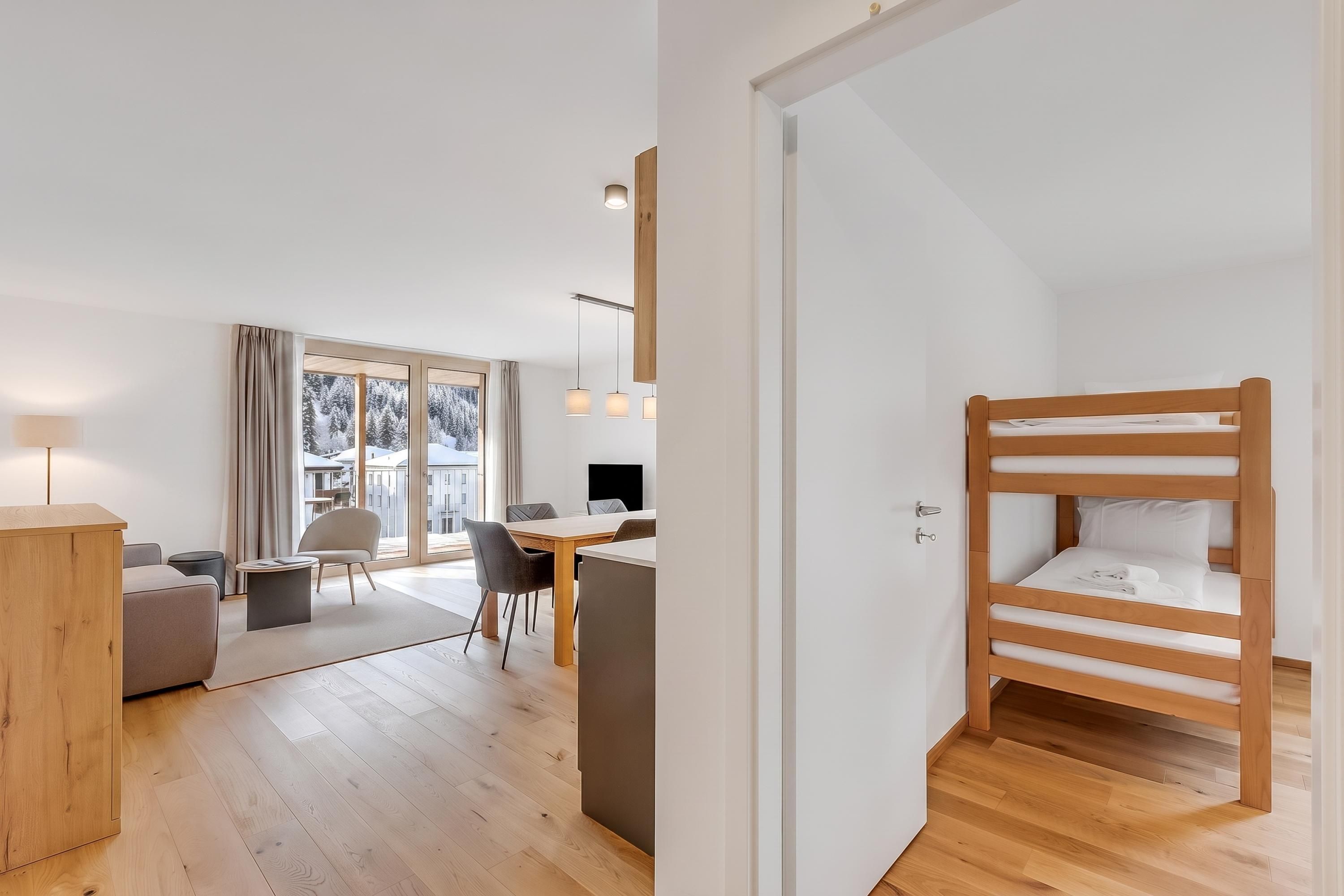 Ein modernes Schlafzimmer mit Etagenbett, Schreibtisch und Blick auf eine verschneite Landschaft durch große Fenster.