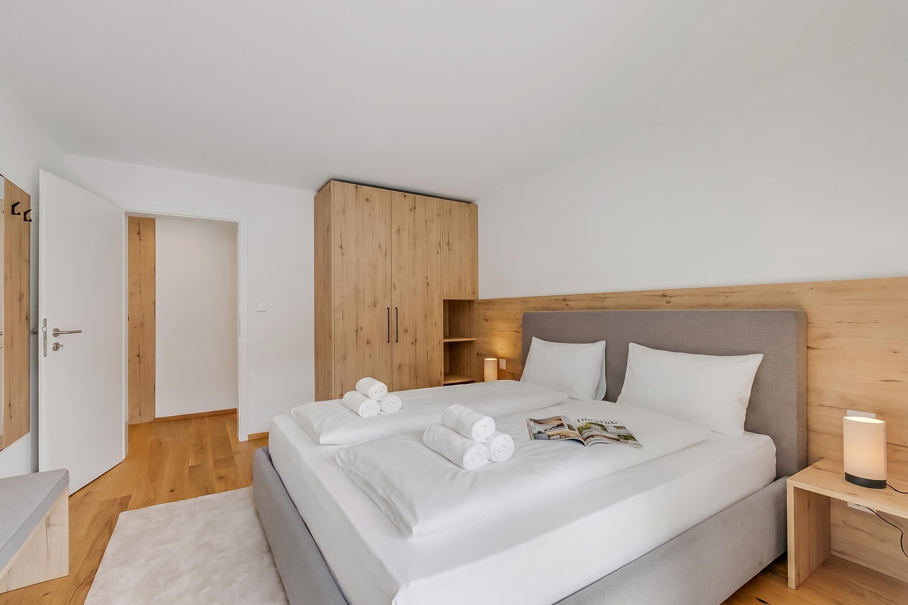 A modern bedroom with a bed, wooden wardrobe, bedside table, and a nightstand.