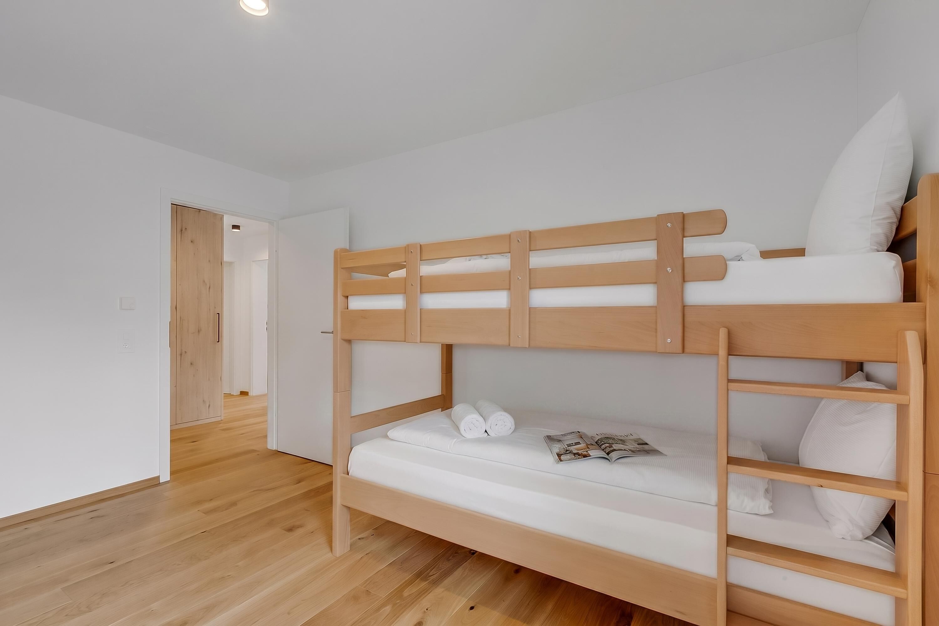 A bunk bed with a wooden frame, white bedding, and a small door in the background.