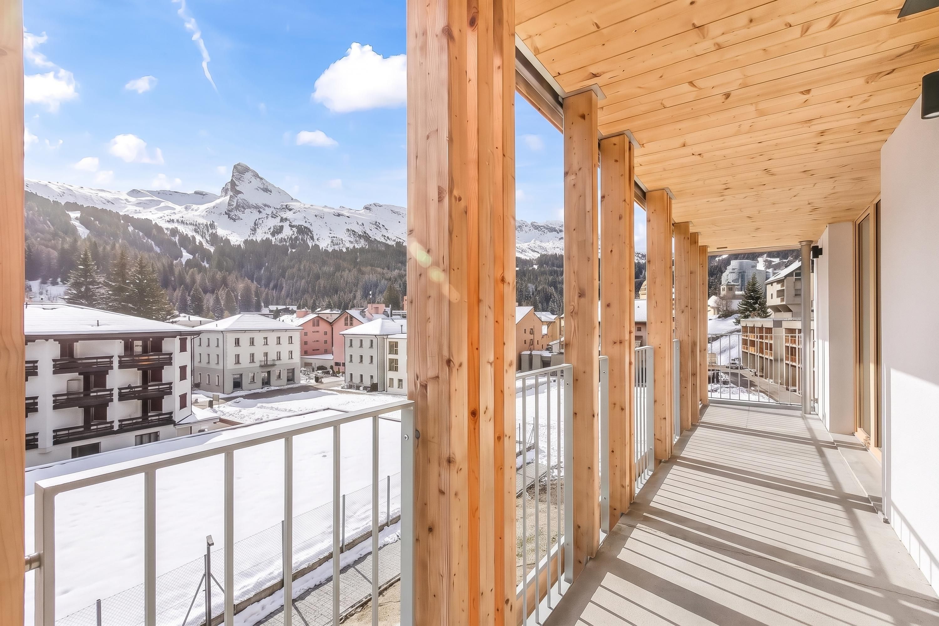 A wooden balcony with a view of a snowy mountain and buildings.