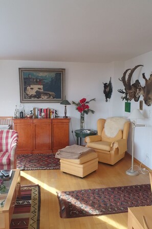 A living room with a sofa, armchair, ottoman, bookshelf, and a painting on the wall. - Oberlech in Lech by Interhome (Lech)