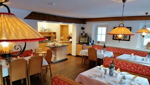 A restaurant with multiple dining areas, including booths and tables, with overhead lamps and a kitchen in the background. - nahe den Skigebieten und Ausgangspunkt zu Sehenswürdigkeiten by Interhome (Mittersill)