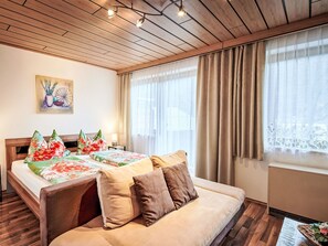 Et hotelværelse med træloft, en seng med blomstret sengetøj, en sofa og et vindue med gardiner.
