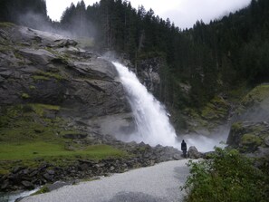 Ein Wasserfall stürzt über einen steinigen Hang, eine Person steht am Fuße.