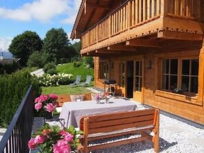 Eine Holzhütte mit Balkon, einem Tisch mit Stühlen und einem Garten voller Blumen.