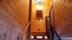 Interior de madera con una escalera que lleva a una zona superior, un candelabro y un ventanal pequeño.