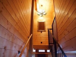 Ein Holzinnenraum mit einer Treppe zu einem Erkerbereich, einer Kandelaberleuchte und einem kleinen Fenster.