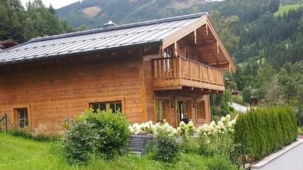Una cabaña de madera con balcón, rodeada de abundante vegetación y colinas.