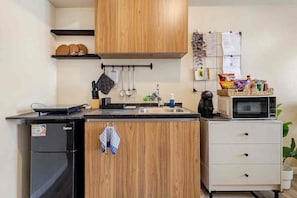 A compact kitchen with wooden cabinets, a black refrigerator, a microwave, and a sink. - Studio Lune | Modern Makati Studio | Queen Bed | Fast Wi-Fi | Self Check-in ⭐ (Makati City)