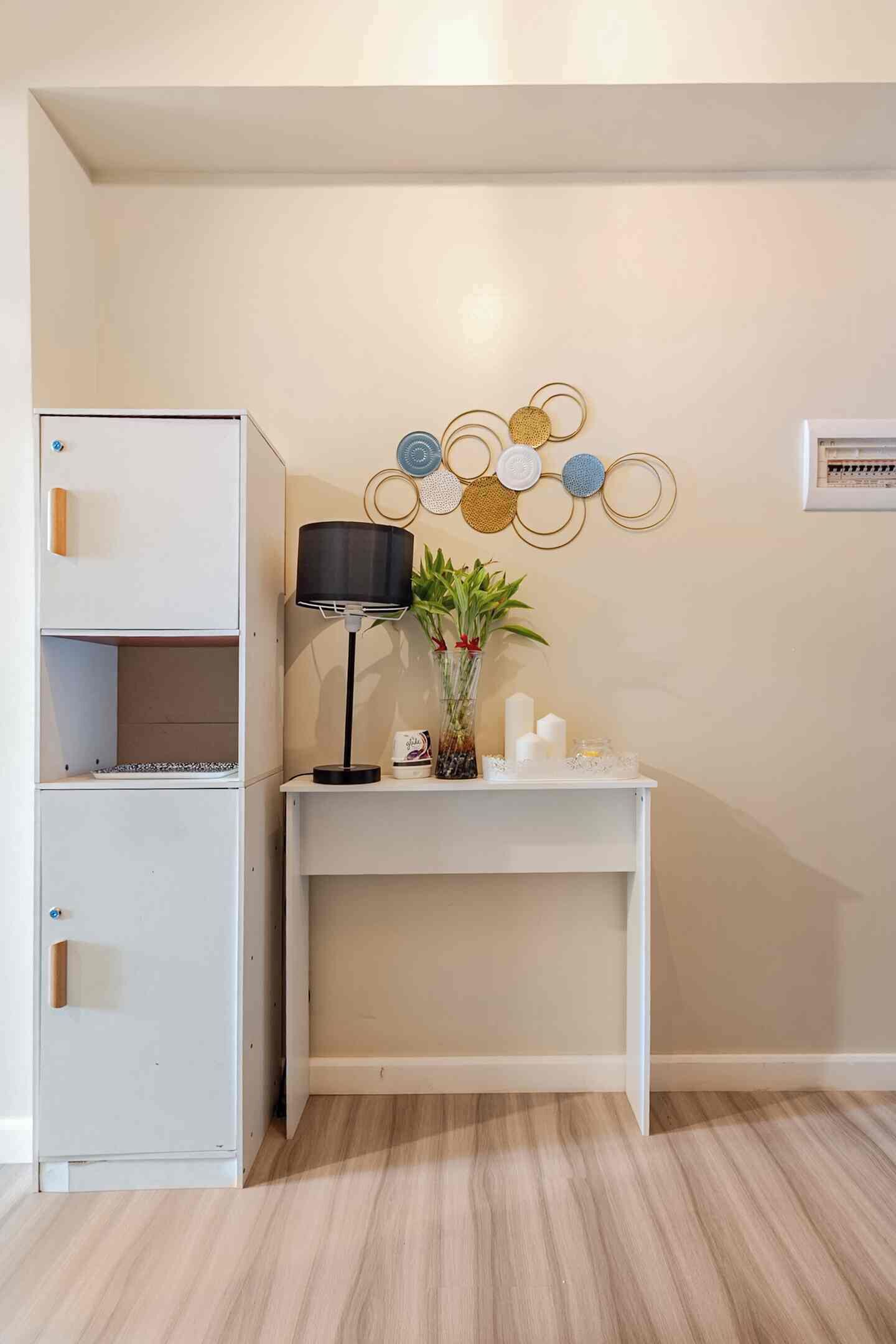 Ein Zimmer mit weißem Schreibtisch, einer Lampe, einem Wanddekor und einem weißen Aktenschrank.