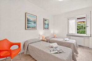 Ein Schlafzimmer mit zwei Betten, einem Sessel, einem Fenster mit Blick auf Grünflächen und zwei gerahmten Bildern an der Wand.