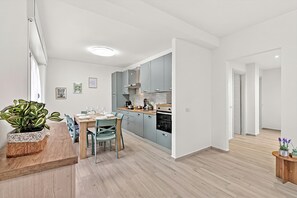 Uma cozinha moderna com armários azul-claros, uma mesa de jantar de madeira com cadeiras e uma planta em vaso à esquerda.
