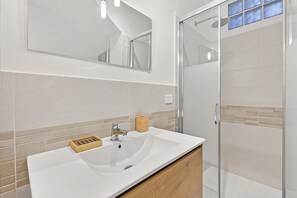 Ein modernes Badezimmer mit einem weißen Waschbecken, einem Spiegel und einer Duschkabine.