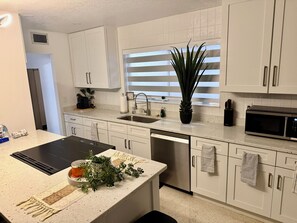 A modern kitchen with white cabinets, a stainless steel sink, a microwave, and a dishwasher. - Charming 3-bedroom house with pool in beautiful Palm Bay (Palm Bay)