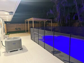 An outdoor swimming pool with a blue light, a covered seating area, and an air conditioning unit. - Charming 3-bedroom house with pool in beautiful Palm Bay (Palm Bay)