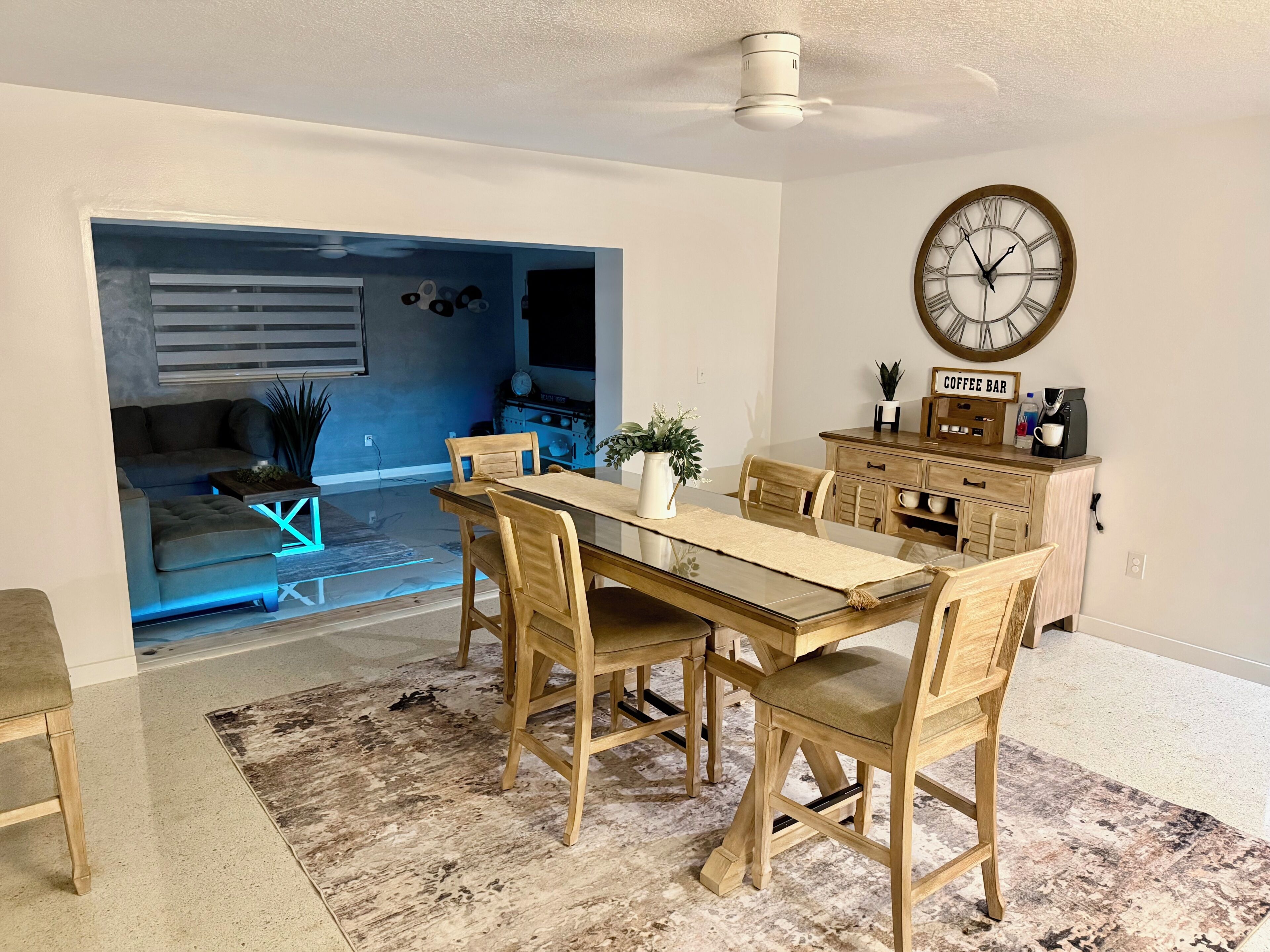 A dining area with a wooden table and chairs, a coffee bar with a clock, and a blue accent wall.