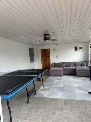 A room with a ping pong table, a grey sofa, and a ceiling fan. - Charming 3-bedroom house with pool in beautiful Palm Bay (Palm Bay)