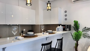 A modern kitchen with white cabinets, a white countertop, two black chairs, a potted plant, and a microwave. - F11 Appartement Douillet à La Marsa (La Marsa)