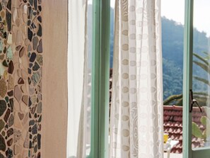 Une fenêtre donnant sur un paysage montagneux, un mur recouvert de carreaux et un rideau à motifs.