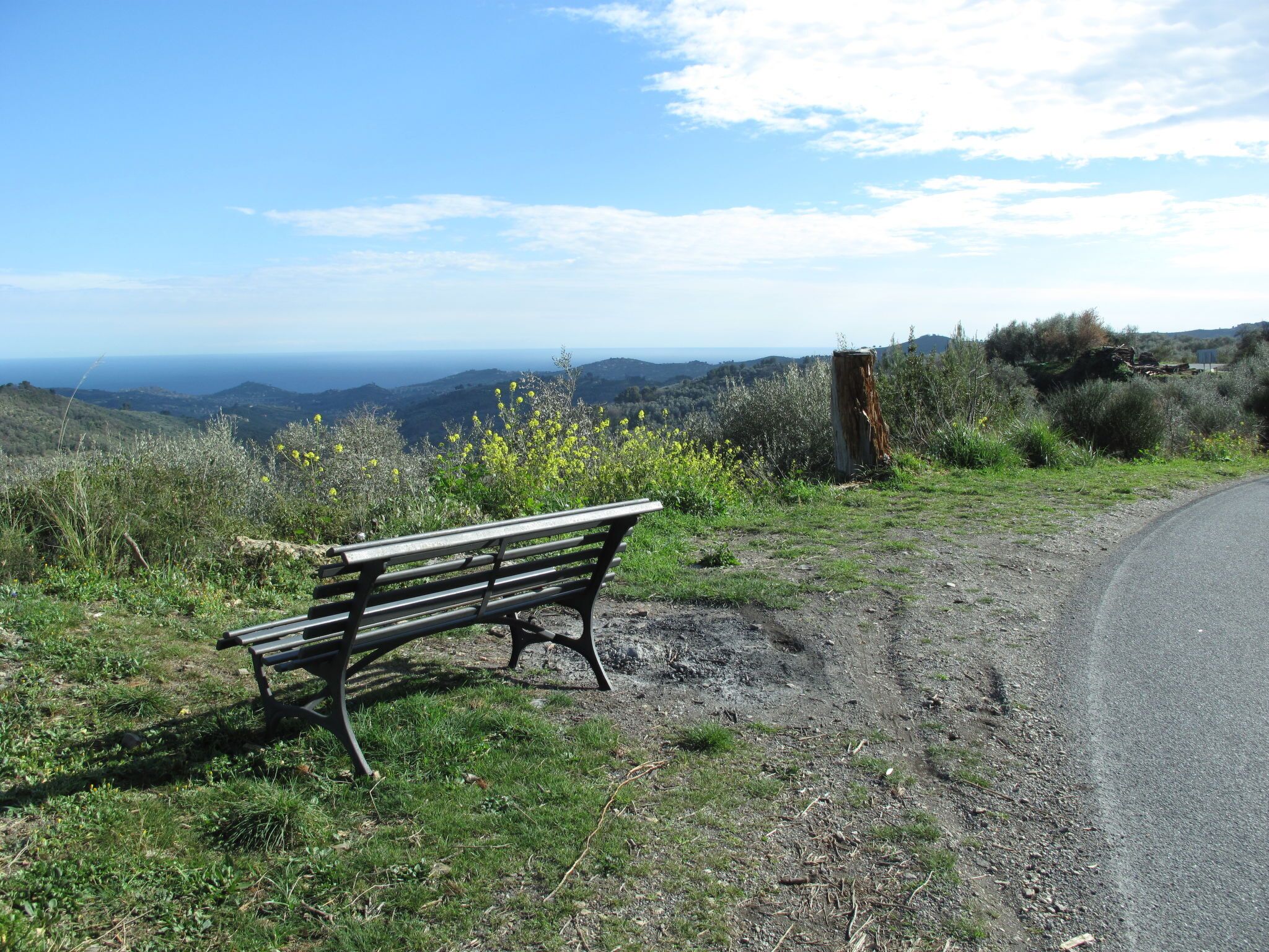Un banc sur une colline verdoyante, avec une route et des collines qui se dessinent à l’horizon.