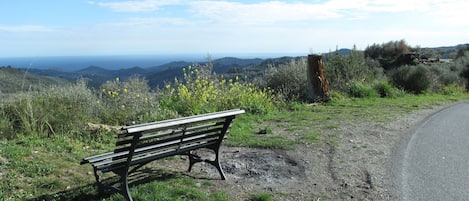 Um banco numa encosta gramada, com uma estrada e colinas ao longe.