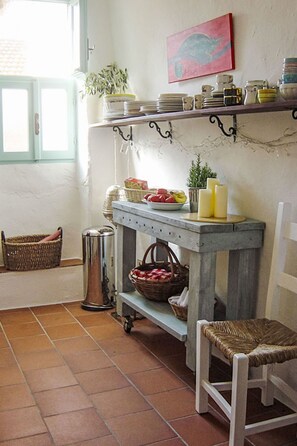 Une cuisine avec un plan de travail en marbre, une étagère suspendue où sont posées des assiettes, un panier en osier et une chaise.