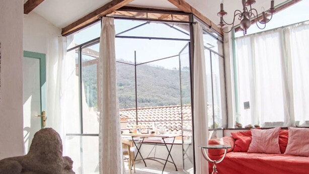 A room with a red sofa, a small round table, and a view of a mountainous landscape through a glass door. - Due Anime Felice by Interhome (Vasia)