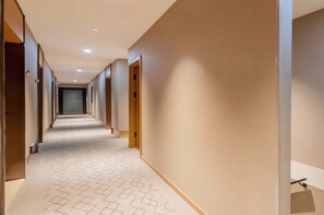 A hotel corridor with a geometric patterned carpet, wooden doors, and recessed lighting. - Baman Hotel  (Beijing)