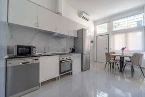 A modern kitchen with stainless steel appliances, a dining area with a table and chairs, and a window providing natural light. - Portazgo Apartment | 2 Bedrooms + Sofa Bed (Madrid)