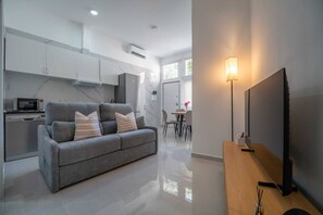 Un soggiorno moderno con un divano grigio, una televisione a schermo piatto e un'area pranzo con tavolo e sedie.